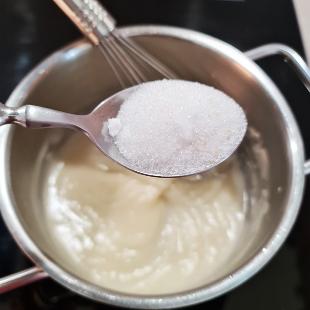 Ein Löffel voll Zucker über Kochtopf